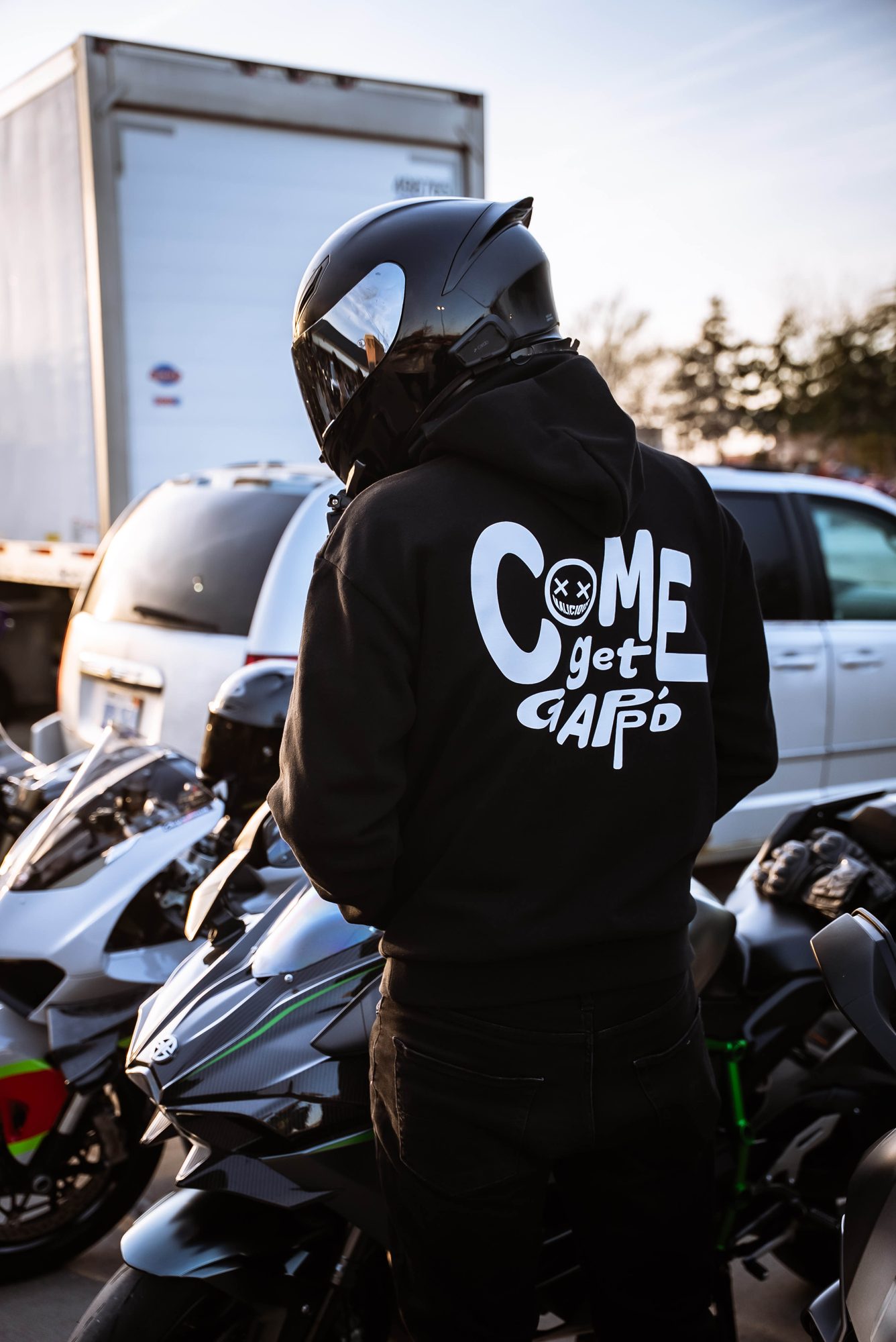 Person in a helmet wearing the Come get Gappd hoodie near motorcycles